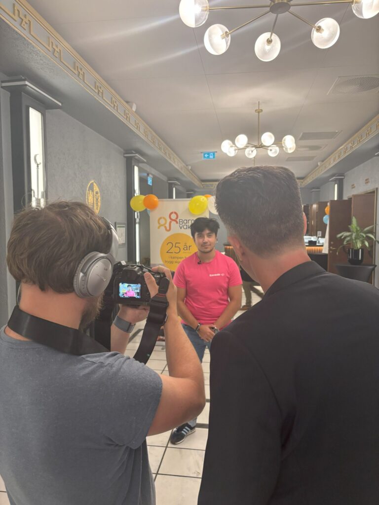 Seks personer iført matchende rosa skjorter poserer på en trapp, noen gjør fredstegn, mens de tar en gruppeselfie i et stort speil.