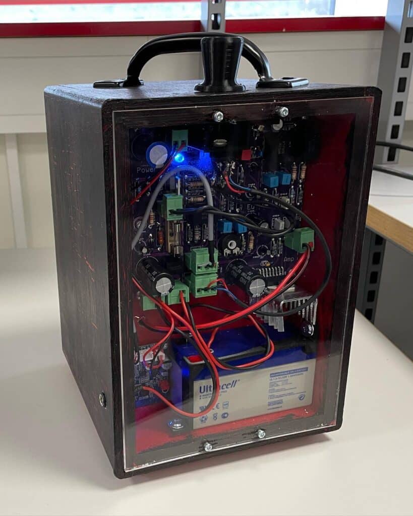 Booster vår2022 (4) En svart boks med gjennomsiktig frontpanel viser elektroniske kretser, ledninger, en blå LED-lampe og et synlig Ultracell-batteri på innsiden.