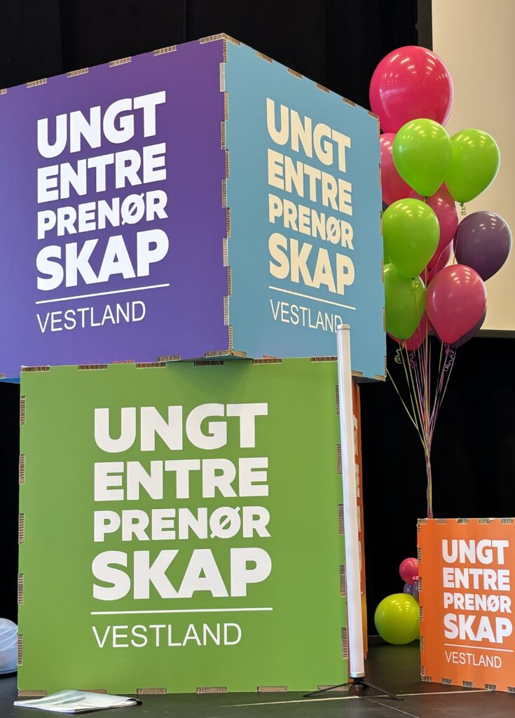 FM UB_2026 (17) Store, fargerike kuber viser "UNGT ENTREPRENØRSKAP VESTLAND" ved siden av ballonger i grønt, rosa og lilla mot en mørk bakgrunn.