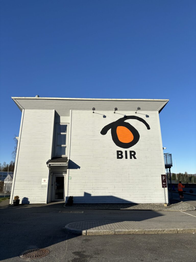 En hvit bygning med logoen og teksten "BIR" på siden, fotografert på en klar, solrik dag med blå himmel.