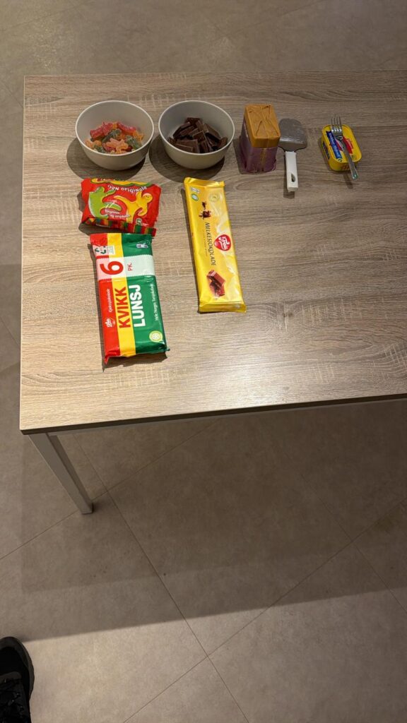 Et trebord med to skåler med snacks, en pizzaskjærer, en pakke smør med gaffel og tre pakker med sjokolade og vafler på.