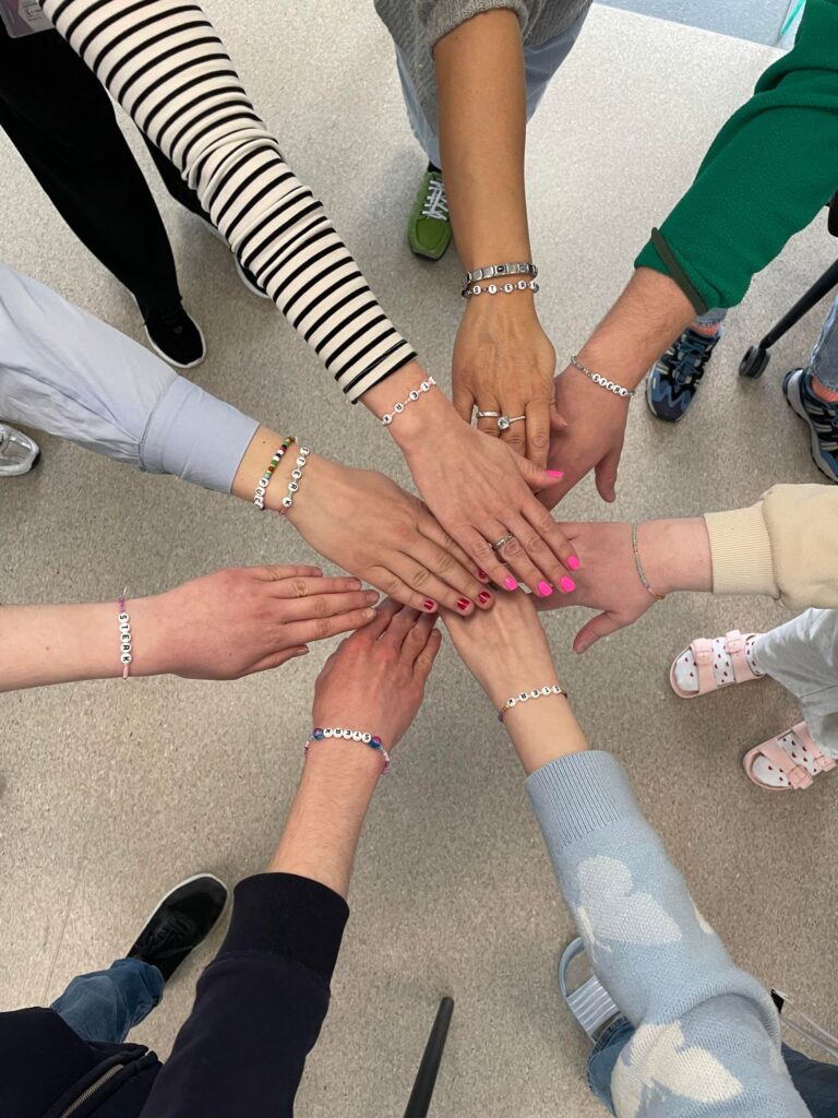 PsykiskHelsedag-04042024-7 Flere personer står i en sirkel med hendene stablet i midten, alle iført matchende perlearmbånd.