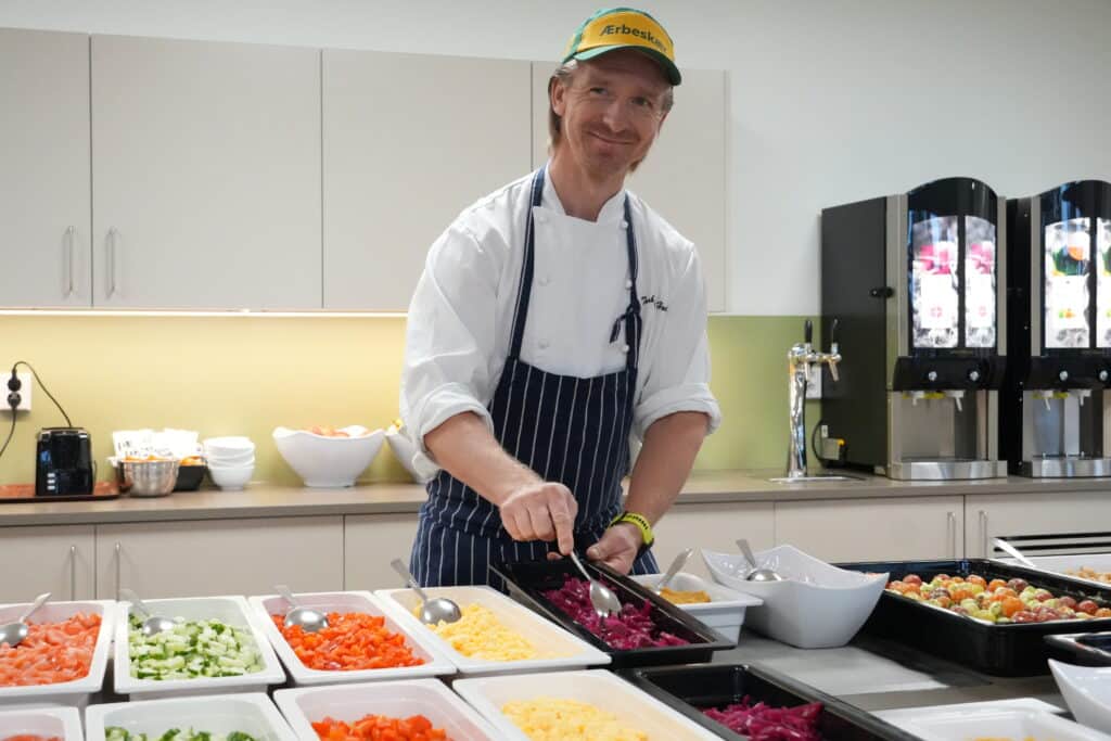En kokk i hvit uniform og grønn lue serverer syltet rødkål fra en salatbar.
