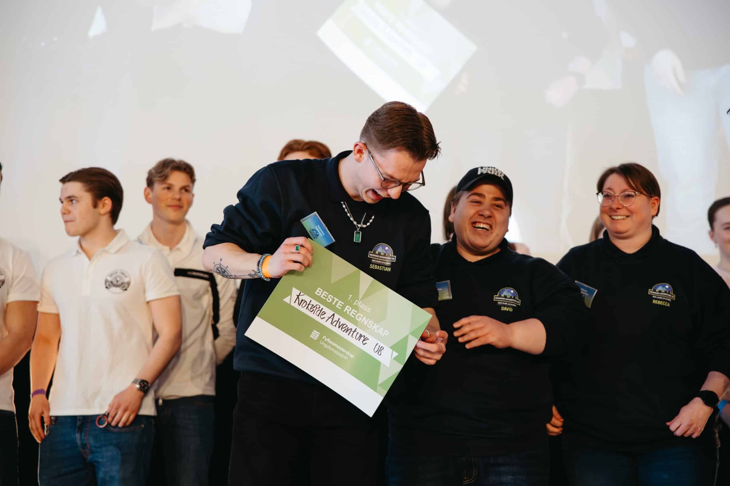 En gruppe mennesker står smilende på scenen. En person i midten holder et "Beste anbefaling: Xplore Adventure UK"-sertifikatet.