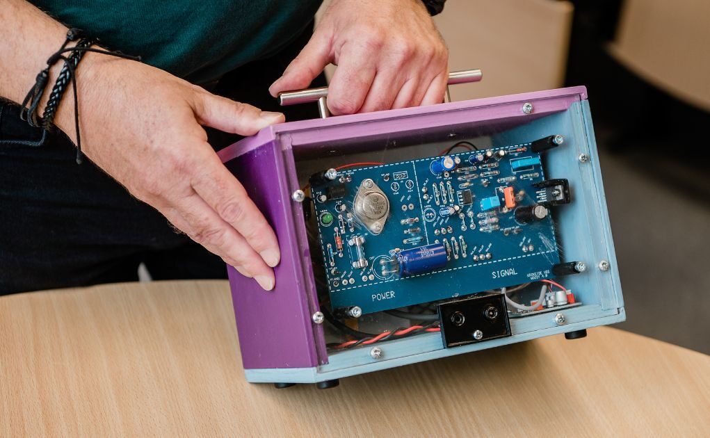 En person holder en åpen, lilla elektronisk enhet som viser interne kretser og komponenter på et bord.