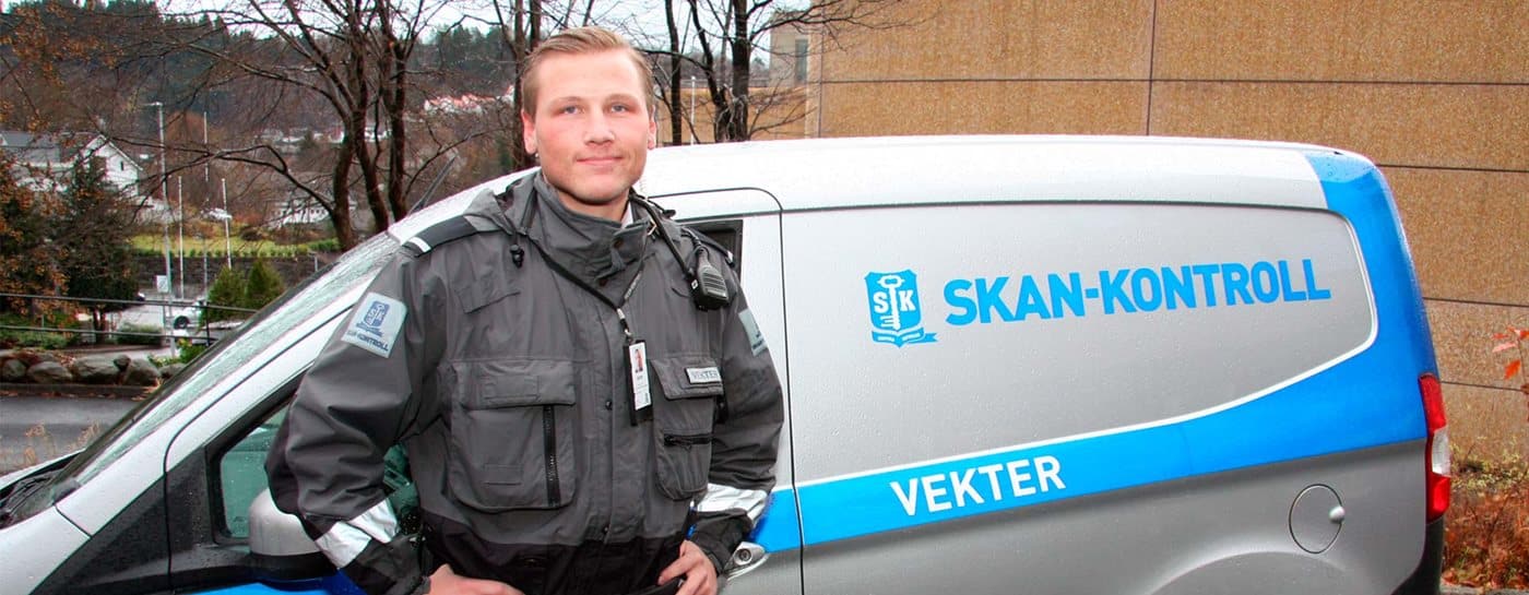 En sikkerhetsvakt står ved siden av en SKAN-KONTROLL-varebil merket "Vekter" på en parkeringsplass.