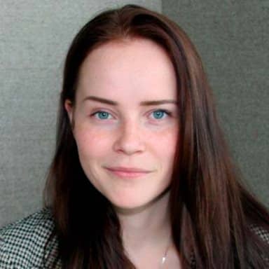 En kvinne med langt brunt hår og blå øyne ser lett smilende inn i kameraet, med en nøytral bakgrunn.